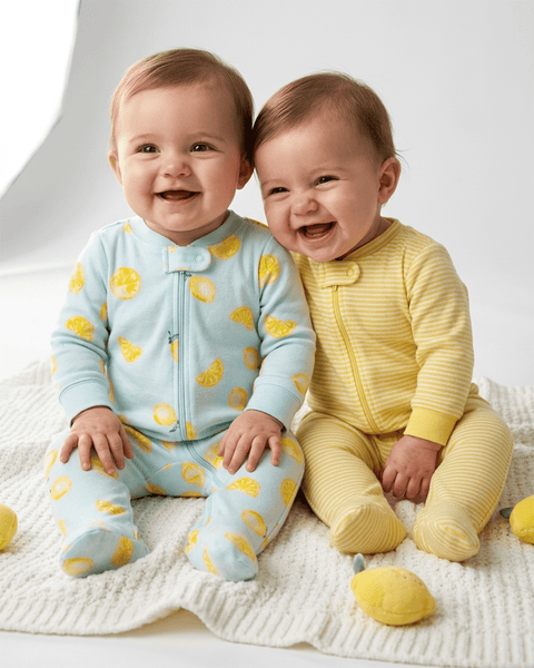 Dos bebés felices usando pijamas Carter's de algodón: uno con estampado de limones y otro de rayas.