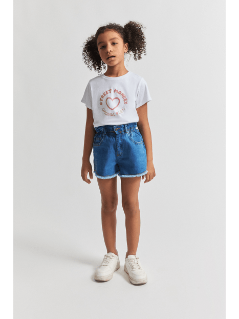 Niña posando con blusa blanca Street Monkey de manga corta y shorts de mezclilla en Kinder Guatemala.