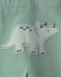 Detalle de un parche de dinosaurio triceratops en color gris claro sobre el pantalón largo verde