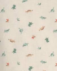 Detalle del estampado de la camiseta con pequeños dinosaurios verdes y terracota sobre fondo crema.