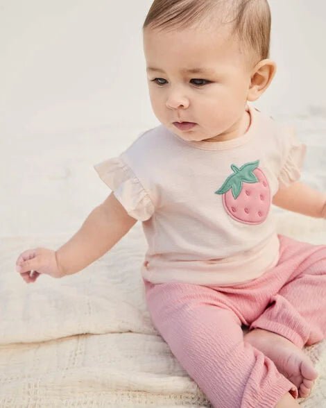 Bebé feliz usando el conjunto Carter's de 3 piezas en rosa claro con camiseta de fresa, gateando
