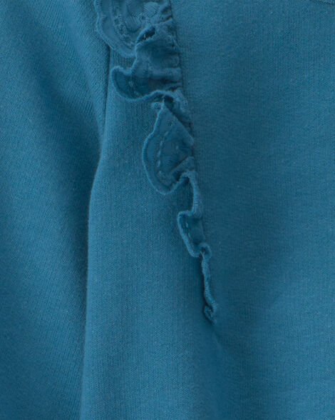 Detalle cercano del hombro del top azul Carter's, mostrando los volantes texturizados y bordados.