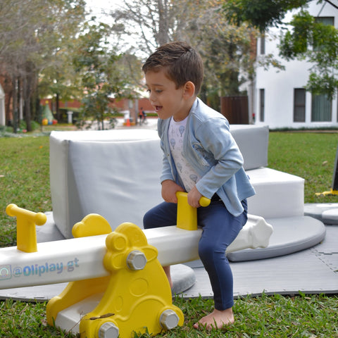 Bebé niño usando conjunto Kinder azul de globos, jugando feliz en un balancín amarillo al aire libre.