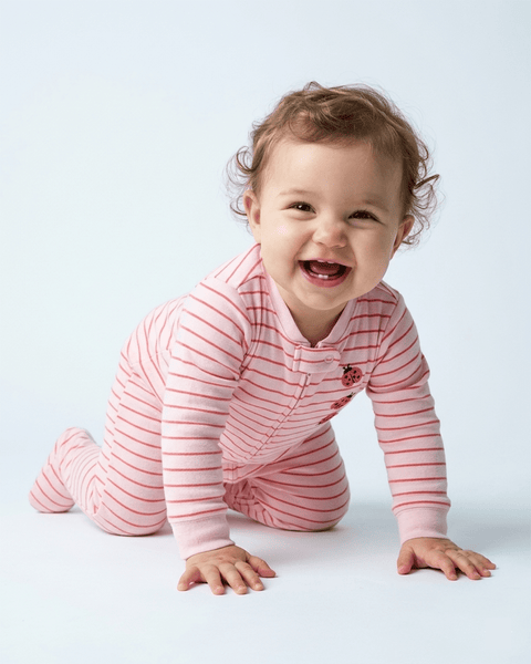 Bebé niña sonriendo y gateando, usando pijama Carter's de algodón rosa con rayas y mariquitas