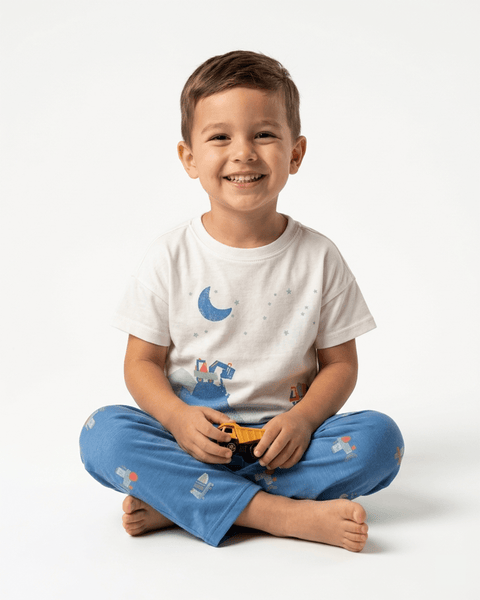 Niño sonriente usando pijama Carter's de camiones de construcción, sentado con las piernas cruzadas.