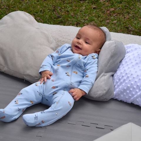 Bebé sonriente recostado, usando pijama azul de vehículos con pies integrados