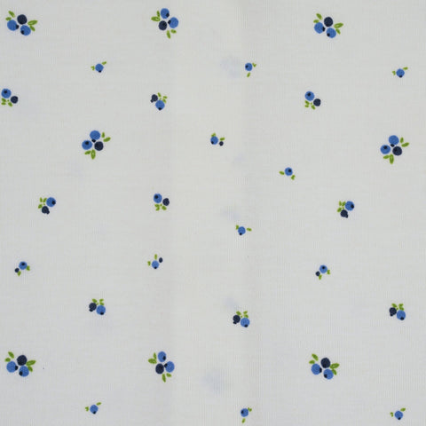 Detalle de estampado de arándanos azules y hojas verdes en la pijama blanca de bebé Kinder.