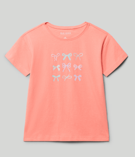 Camiseta de jersey Blue Seven color coral para niña con estampado de moños turquesa en el frente.