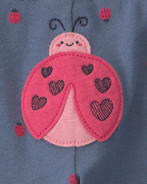 Detalle de pantalón azul grisáceo con aplique grande de mariquita rosa y corazones negros.