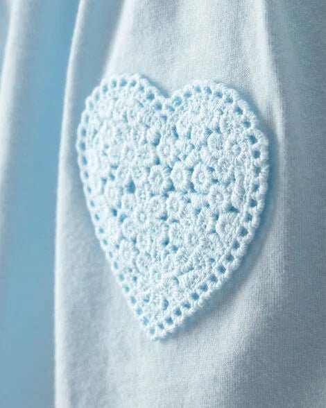 Detalle de corazón crochet celeste bordado en el bolsillo del enterizo Carter's para bebé.