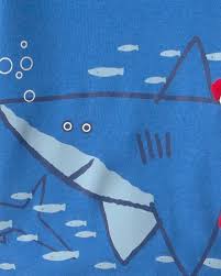 Primer plano de camiseta de pijama azul claro con diseño de tiburón grande y peces pequeños.